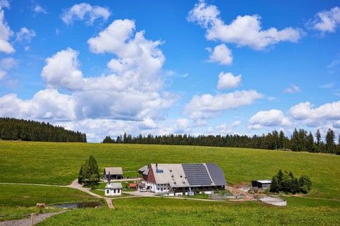 Farmstead with solar cells in a landscape with meadows and forest under a blue sky with cumulus