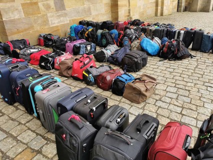 The luggage of a group of travellers stands in rows on the pavement, outside, suitcases and bags