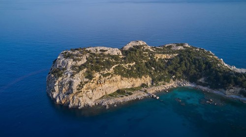 Drone shot, Steep rocky island with dense vegetation surrounded by clear blue sea, Anthony Quinn