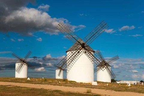 White windmills under a clear blue sky with scattered clouds. The surroundings are brightly lit and