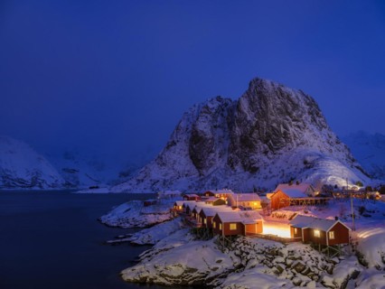 Rorbuer huts of Hamnoy at the fjord at dusk, snowy mountains in the background, Hamnøy, Reine,