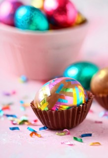 Small chocolate Easter eggs wrapped in shiny foil, placed on a bed of shredded pastel-colored