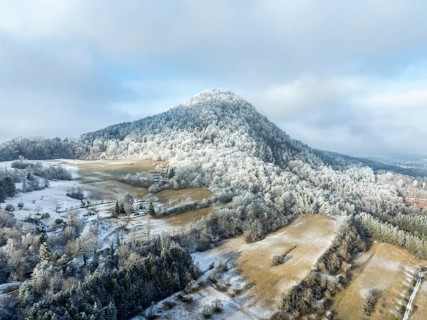 Aerial view of the snow-covered Hegau volcano Hohenhewen, surrounded by frosty trees in a winter