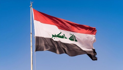 The flag of Iraq flutters in the wind, isolated against a blue sky