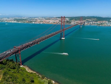 Red bridge spanning the water, lined with boats, with a city and nature in the background on a
