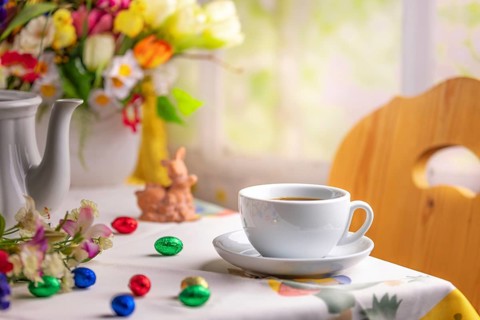 A coffee cup on a table with Easter decorations and a colourful bouquet of spring flowers in the