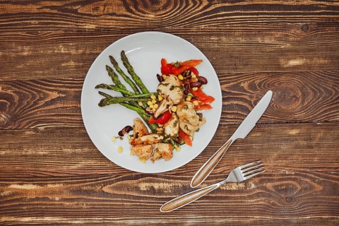 Overhead view of spicy chicken stew with vegetables and fried asparagus on wooden table