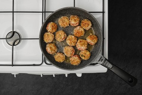 Top view of cooking meatballs in frying pan with olive oil on a gas stove