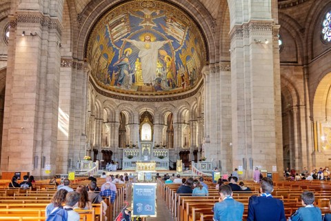 Church interior with a large mosaic of Jesus above the altar, people praying, Paris