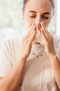 Woman in bright room uses paper towel, focus is on facial expression of discomfort, 'symbolic