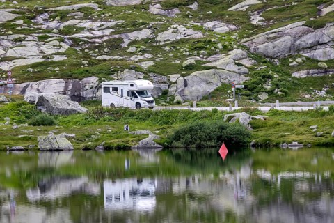 Gotthard Pass, top of the pass. A motorhome is reflected in a mountain lake. Airolo, Canton Ticino,