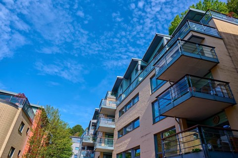 Modern residential building with several balconies and glass railings under a blue sky with clouds