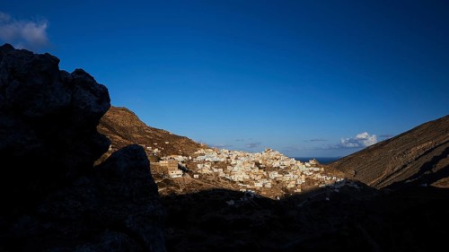 A village in the early morning light, surrounded by dark hills and rocks, illuminated by moon or