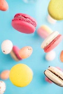 Multicolored flying macaroons and chocolate eggs frozen in the air on blurred blue background. top
