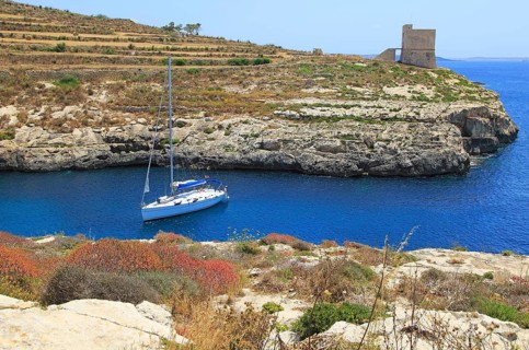 Yacht and watchtower at entrance to Mgarr ix-Xini coastal inlet, island of Gozo, Malta, Europe