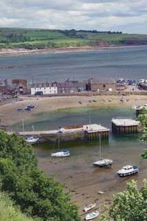 Coastal village with beach, boats and houses surrounded by green countryside, Stonehaven,