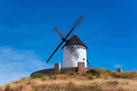 White windmill with black roof on a hill with dry grass under a deep blue sky, Alcazar de San Juan,