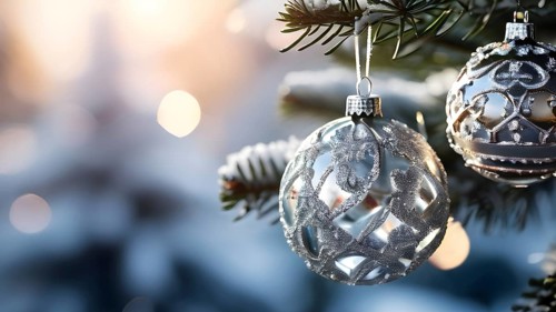 Set of Christmas ornaments hanging on a snow-covered pine tree branch, with frost clinging to the