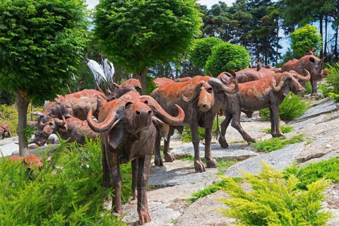Group of metal sculptures depicting buffaloes in a natural setting with trees and shrubs, Bacalhôa,