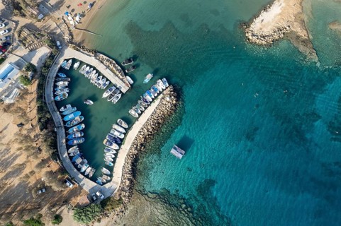 Aerial drone view of fishing harbour and sandy beach. Agia Triada people swimming and fishing boats