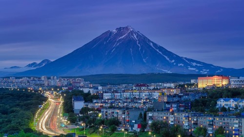 Panorama of night city of Petropavlovsk-Kamchatsky on background cone of volcano, urban development