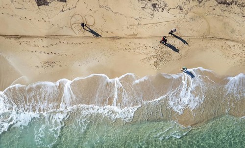 Drone aerial scenery of unrecognised people walking in a sandy beach in winter. Windy waves