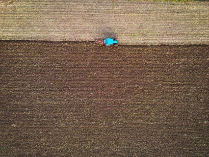 Aerial view of a tractor ploughing a field, a farmer in a modern tractor ploughing field on a sunny
