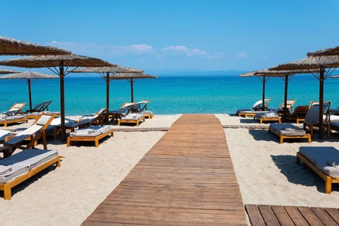Wooden walkway leads to a sunlit beach with deckchairs and parasols by the clear sea, Lago Seaside