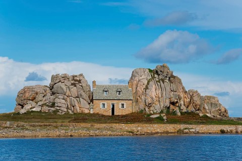 A lonely house between rocky cliffs by the sea and under a blue sky, house between the rocks on the