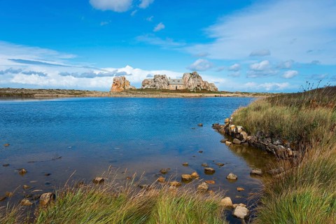 A house stands between rocks on a lake under a blue sky with clouds, House between the rocks on the