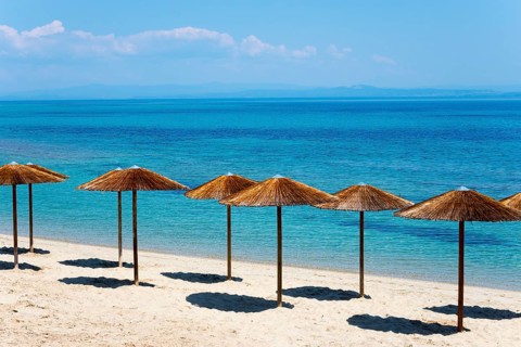 Sandy beach beach with thatched roofs and clear blue sea under a sunny sky, Golden Beach, Pallini,