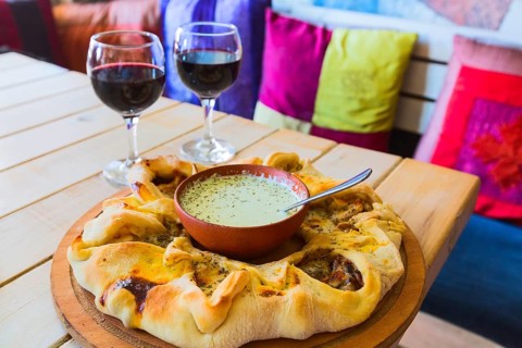 Traditional Georgian adjara round pie with sauce dressing, two wine glasses and sofa with pillows