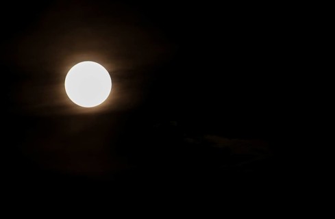 Super bright full moon and partially covered with dramatic black sky clouds