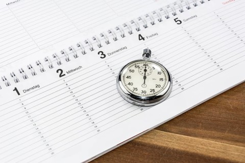 Stopwatch lying on a schedule on a wooden desk (with captions of the days of the week in German)