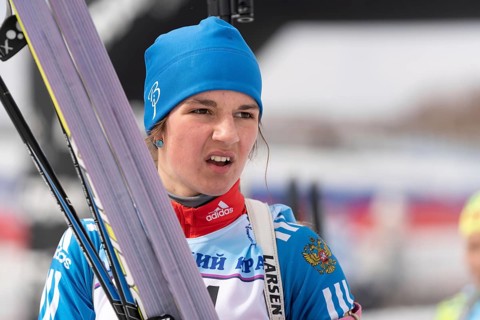 Sportswoman biathlete Soenko Violetta with skis in hands and rifle behind her after skiing and