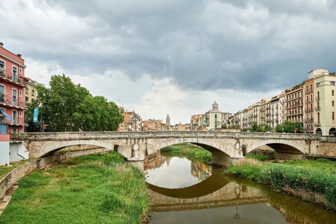 Colorful yellow and orange houses and bridge Pont de Sant Agusti reflected in water river Onyar, in