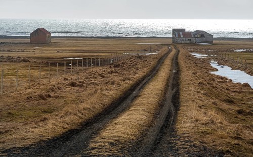 Icelandic meadow land with empty rural road leading to an abandoned farmhouse near the Atlantic