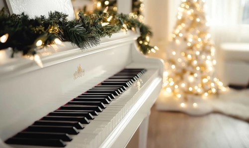 A white grand piano is surrounded by a Christmas tree and a wreath. Scene is festive and joyful, as