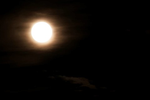 Super bright full moon and partially covered with dramatic black sky clouds