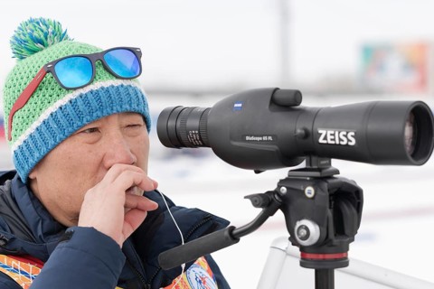 Coach of South Korea biathlon team watches biathletes in monocle at shooting range of biathlon