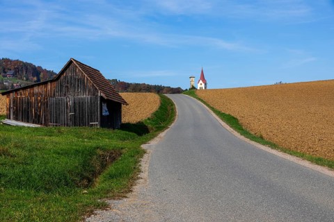 Autumn atmosphere, country road leads through freshly cultivated farmland, church tower and wayside