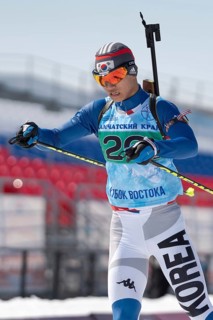 Sportsman biathlete Cheon Yunpil South Korea skiing on ski track distance biathlon arena. Junior