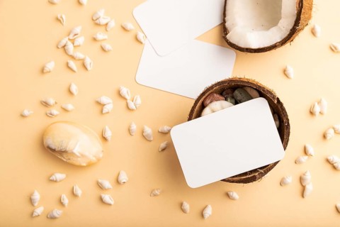 White paper business card with coconut and seashells on orange pastel background. Top view, flat
