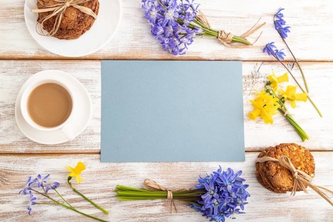 Blue paper sheet with oatmeal cookies, spring snowdrop flowers bluebells, narcissus and cup of