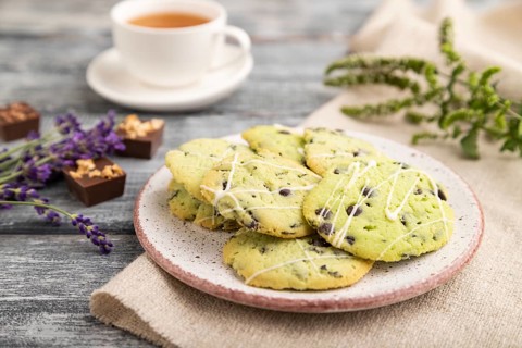 Green cookies with chocolate and mint on ceramic plate with cup of green tea and linen textile on