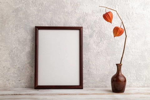 Brown wooden frame mockup with physalis in ceramic vase on gray concrete background. Blank,