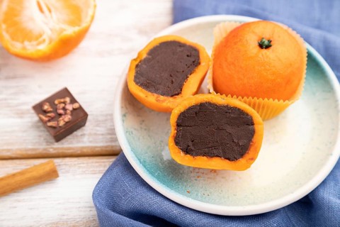 Truffle chocolate tangerine candies on a white wooden background and blue linen textile. Side view,