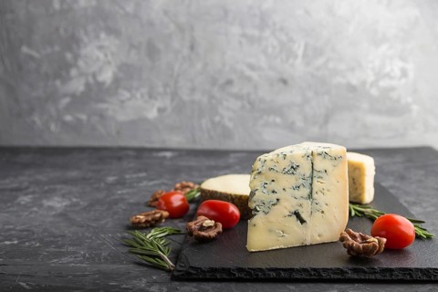 Blue cheese and various types of cheese with rosemary and tomatoes on black slate board on a black