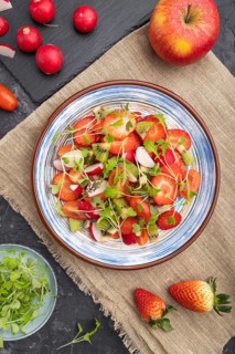 Vegetarian fruits and vegetables salad of strawberry, kiwi, tomatoes, microgreen sprouts on black