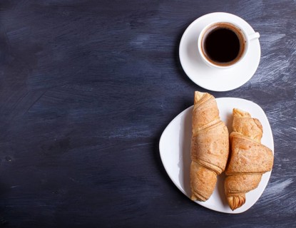 Two croissants with cup of coffee on white plate on black wooden background. top view with